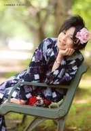 遠矢/膝上・座り・浴衣紫黒・頭に花ピンク・右手ベンチ・左手顔・首傾げ・背景野外/執事歌劇団公式生写真